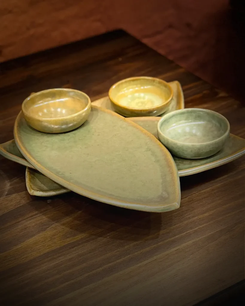 Conjunto de peças de cerâmica artesanal esmaltadas em verde, criadas na Bone Ceramics, sobre mesa de madeira