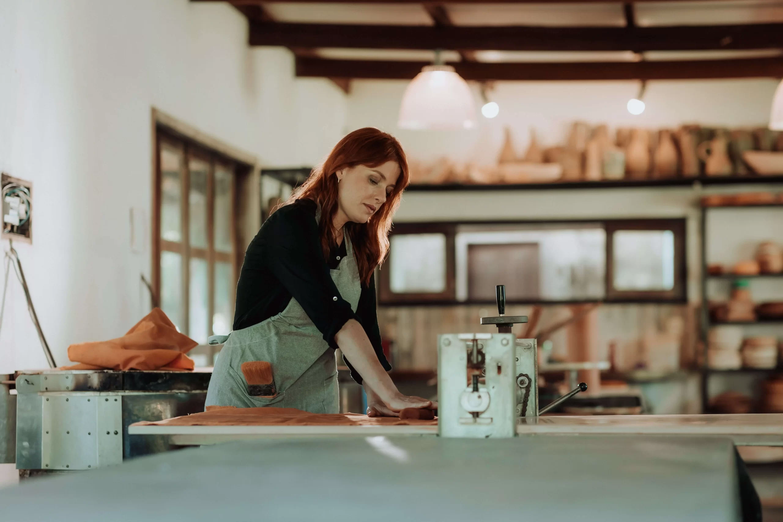 Vívian Vieira modelando argila em bancada no espaço da Bone Ceramics, com ambiente artesanal e iluminação natural